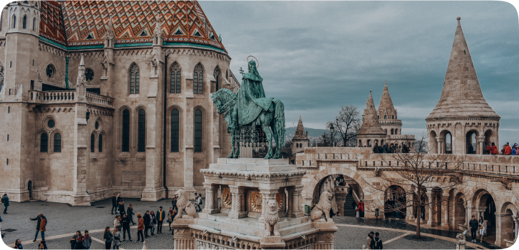 Imagem de uma das diversas praças de Budapeste, com o monumento de uma pessoa em cima de um cavalo, por cima de outras esculturas em mármore.